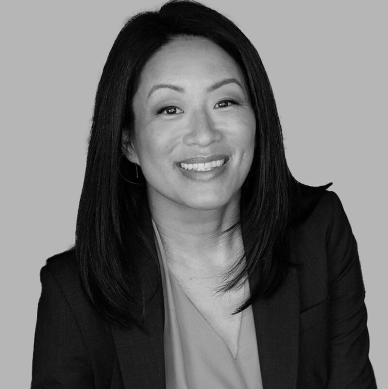 A woman in a suit and tie smiles confidently, showcasing a professional appearance and positive demeanor.