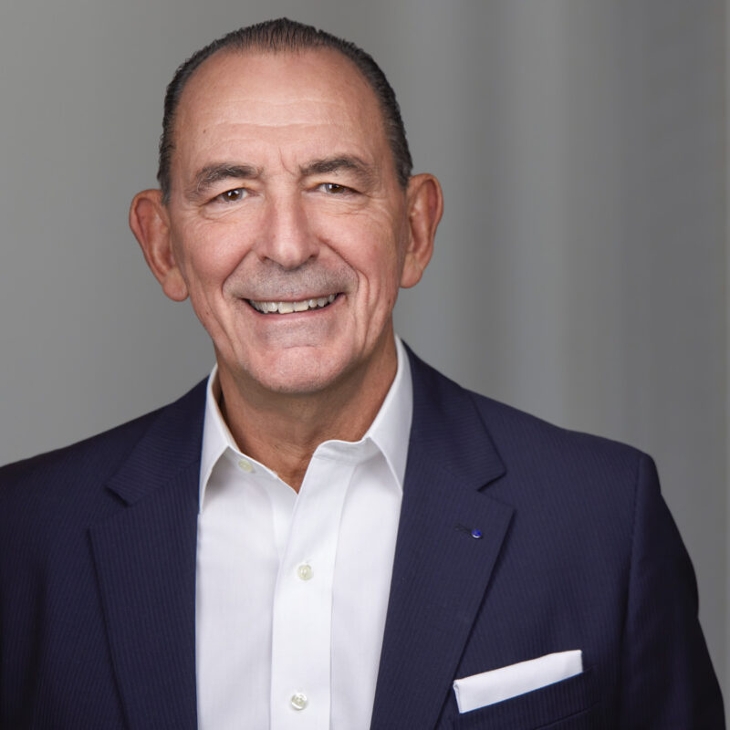 A man in a suit and white shirt smiles confidently at the camera.