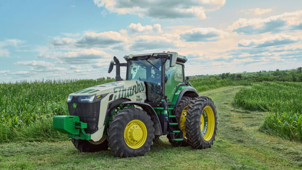 A John Deere tractor in a green field with a blue sky and clouds, the tractor is decorated with Pivot Bio branding and the word "Thanks" for the One Million Thanks campaign